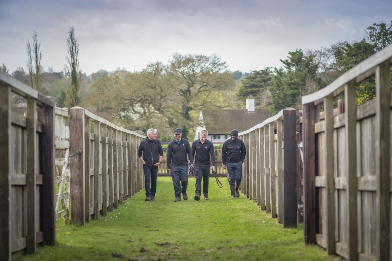 Four people chat and walk on the outskirts of a paddock.